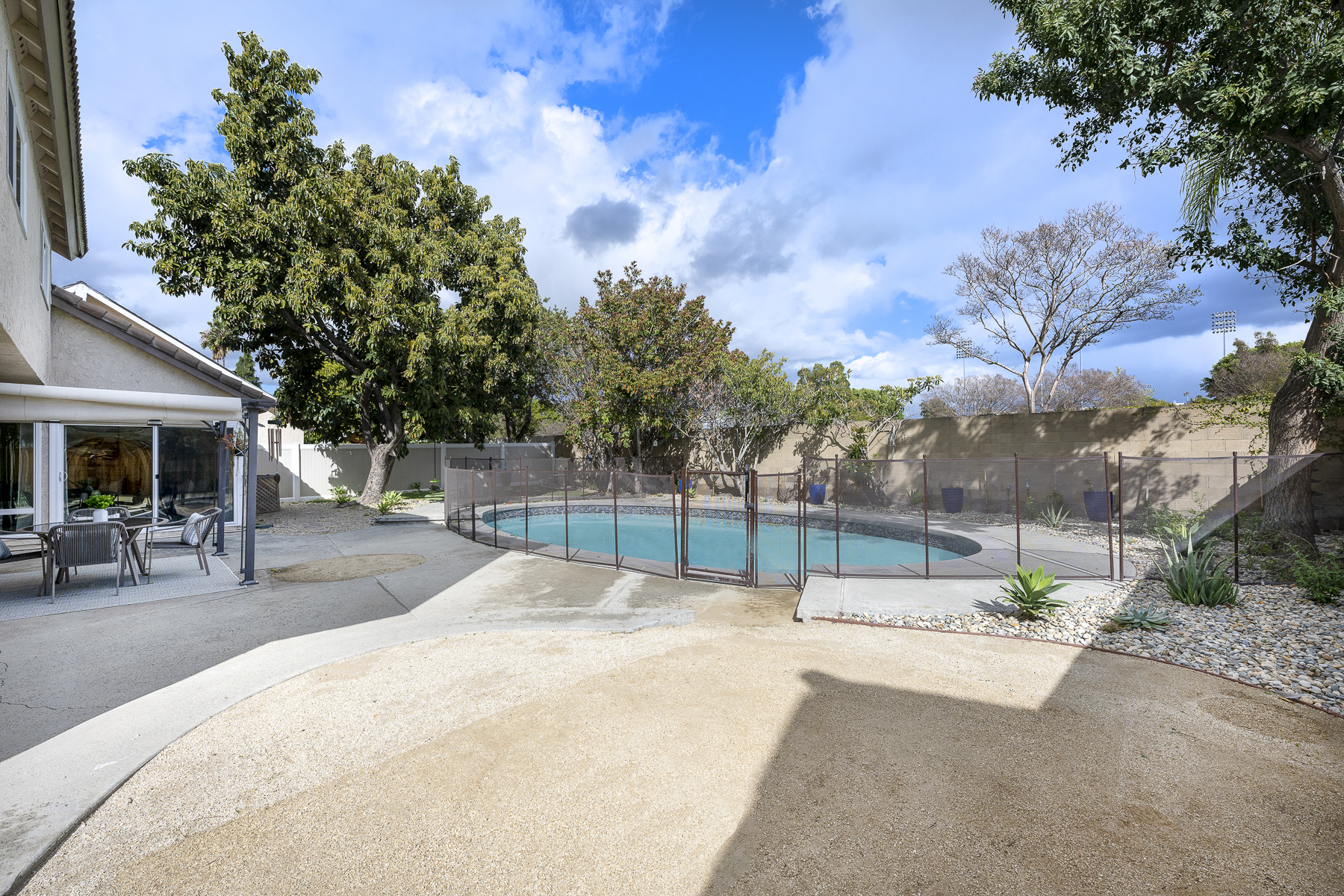 Backyard side view with concrete area, pool and surrounding gate, stone wall, and plants