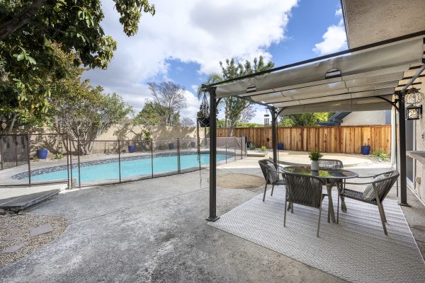 Backyard sitting area under awning with pool and enclosing fence that connects to stone wall