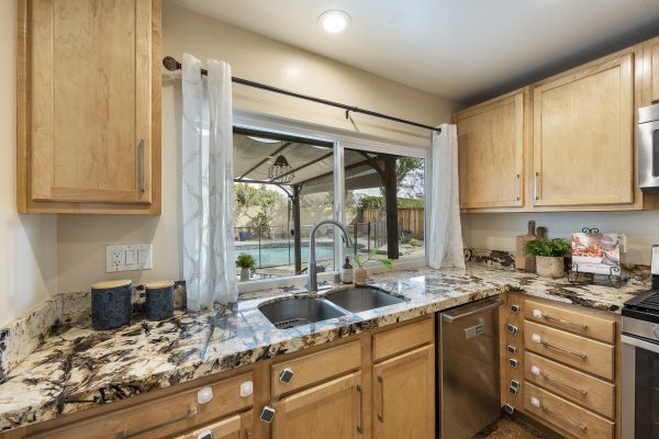 Angled view of kitchen sink, windows, marble counters, cabinets, and dishwasher