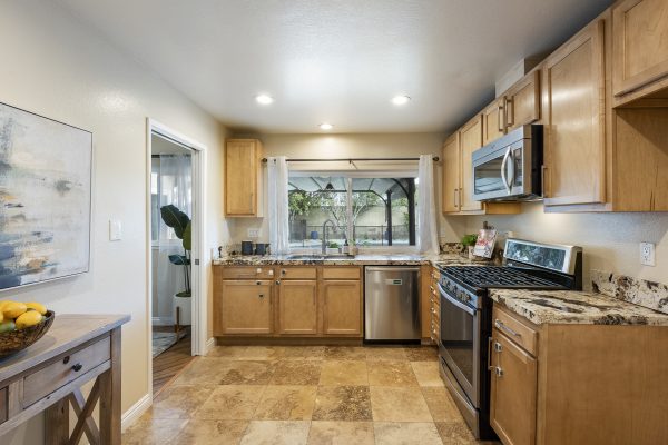 View of L-shaped kitchen counter with dishwasher, oven, microwave, and windows above sink