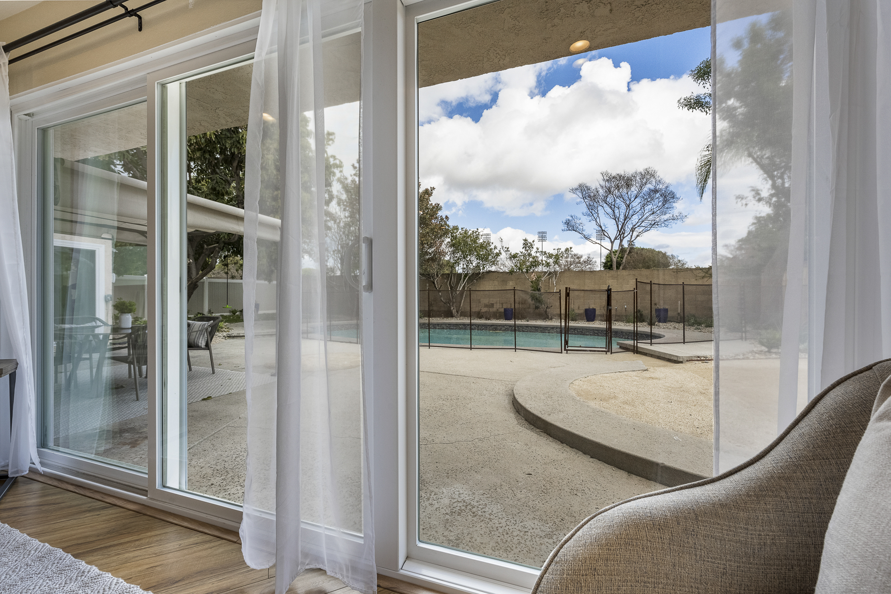 Glass sliding door and windows with view of backyard, including pool and the surrounding gate
