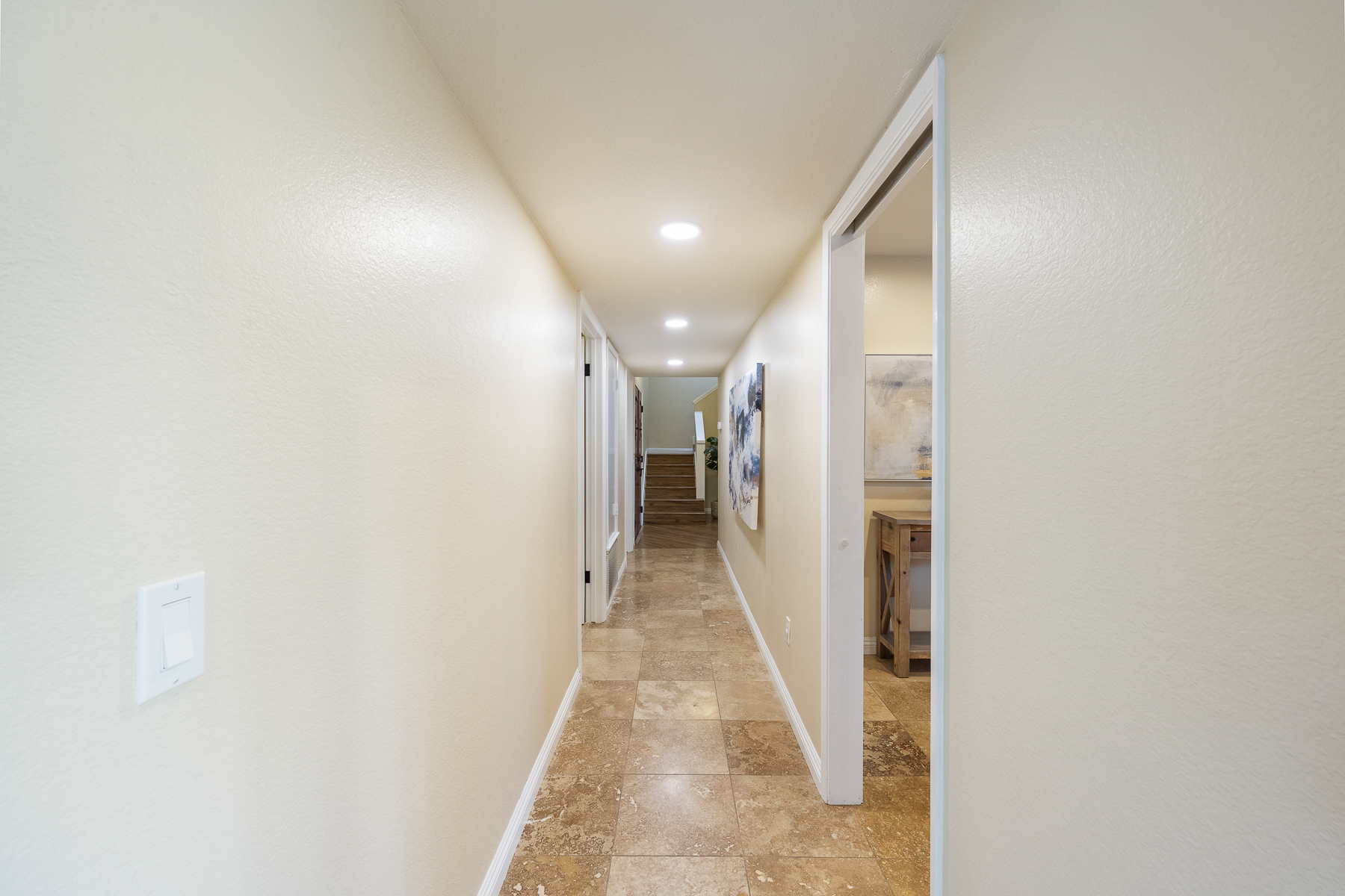 Long hallway with tile flood leading into hardwood stairs